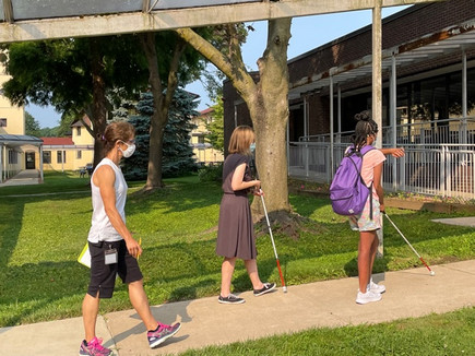 Female student with a cane is followed by two female orientation and mobility instructors.