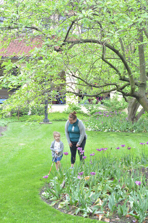Young student using a cane walks on campus with her mother near colorful tulips and beautiful trees.