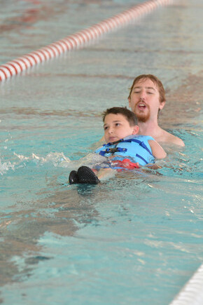 Male student learns to float on his back with male coach behind him in the pool