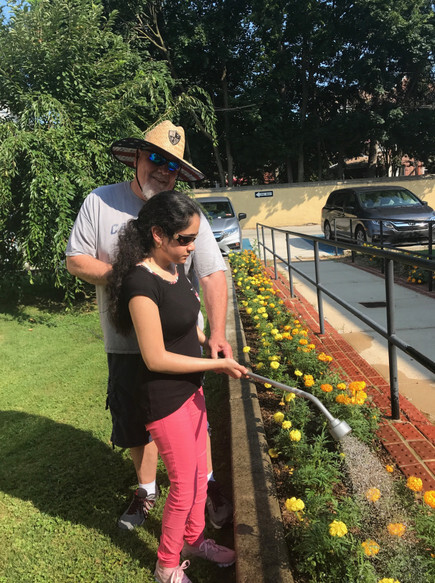 female student waters the flowers with help from male teacher