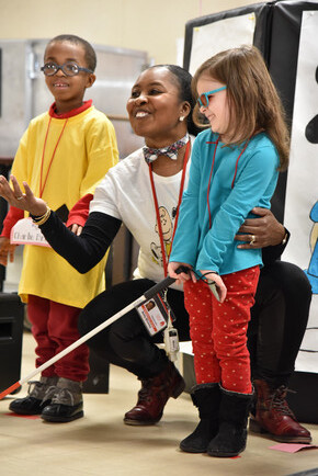 A teacher points to a lesson while a young students holds her cane.