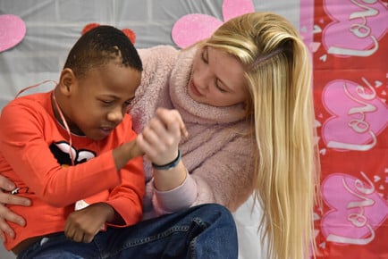 A female teacher holds the hand of a young student.