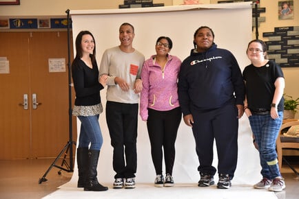 A teacher stands with her students on a photo backdrop cloth.