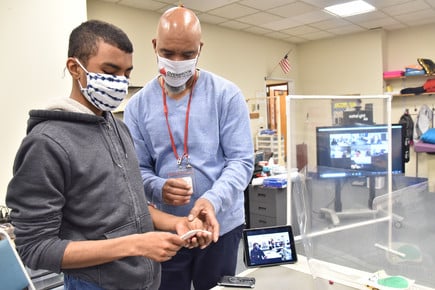 Young male student is assisted by a male teacher.